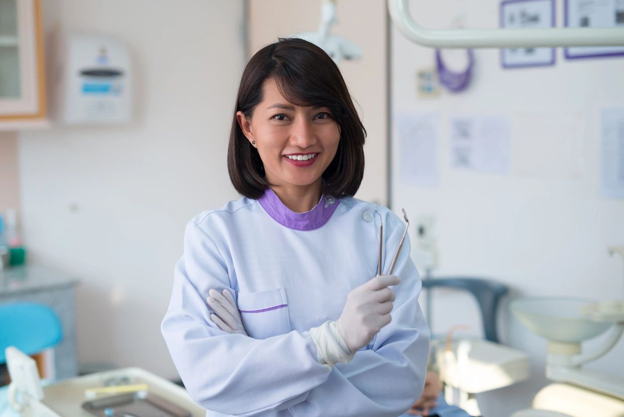 Asian woman dentist stood smiling and holding a dental tool in a hospital.